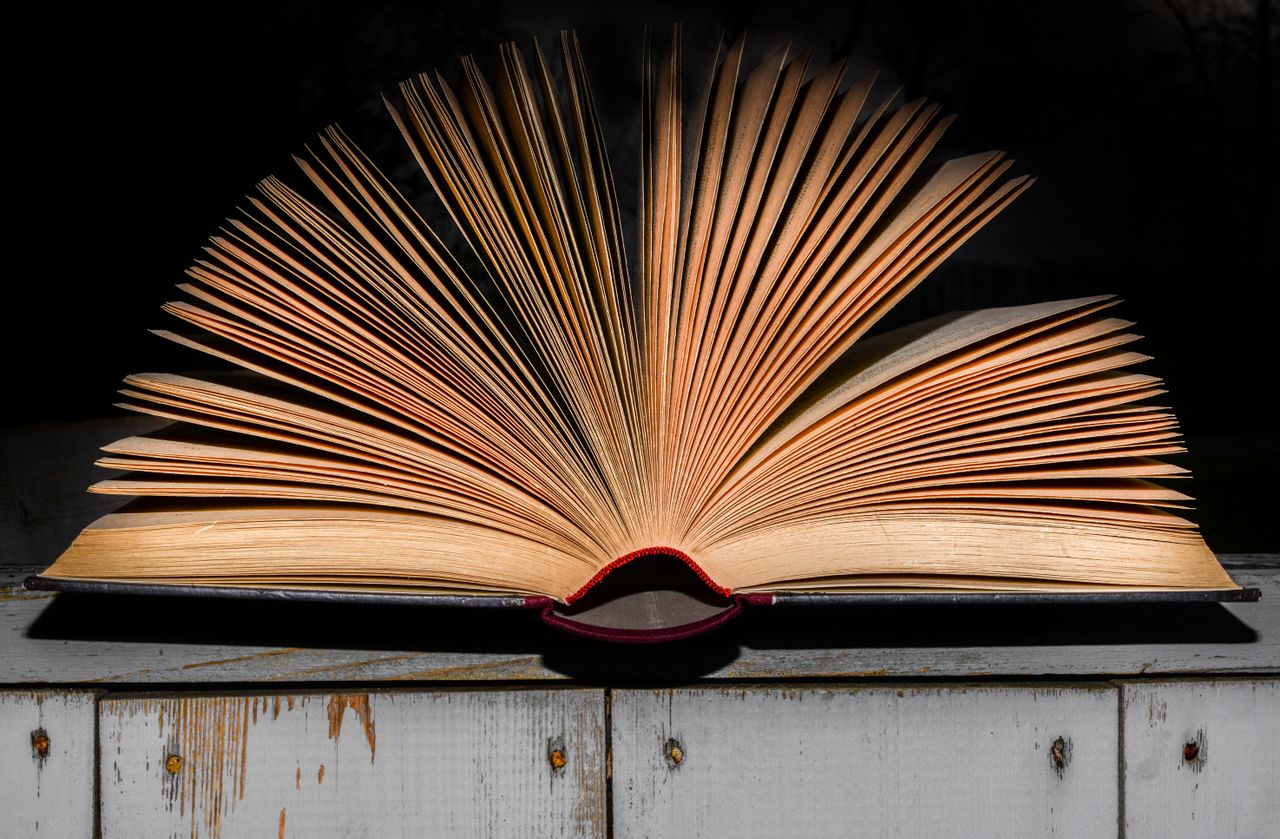 An open vintage book displayed on a wooden surface with dramatic lighting emphasizing its textured pages.